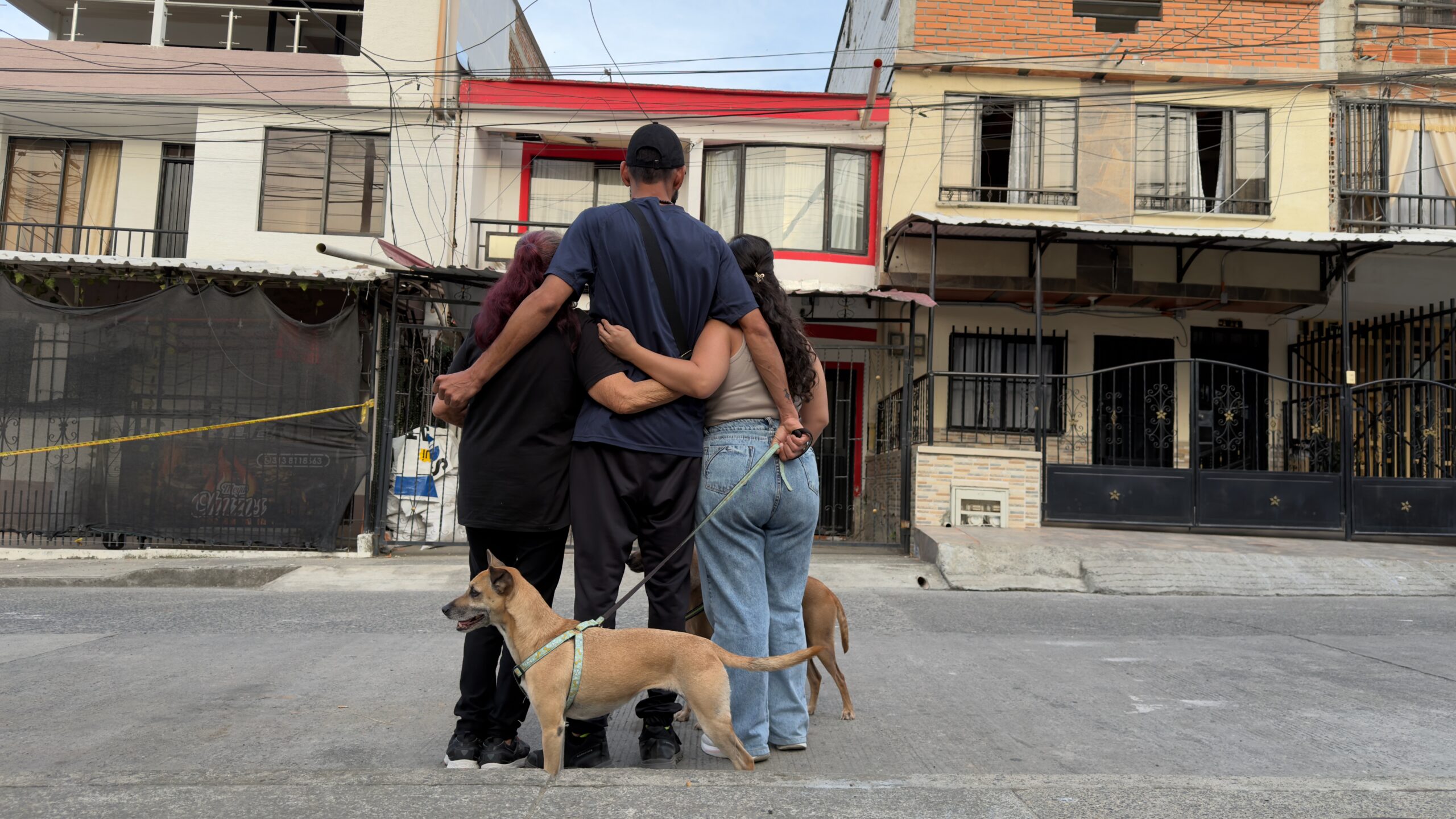 Three people embracing with their dogs outside the home